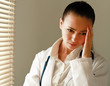 Female doctor with head pain standing near window