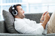 Foto: Man on sofa with headphones and digital tablet Man on sofa with headphones and digital tablet