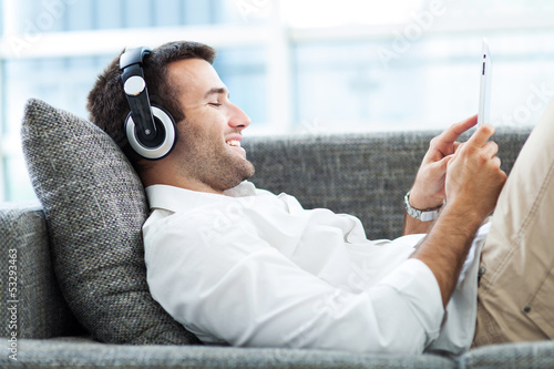 Photo: Man on sofa with headphones and digital tablet Man on sofa with headphones and digital tablet