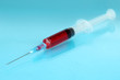 Plastic disposable syringe filled with blood on blue background