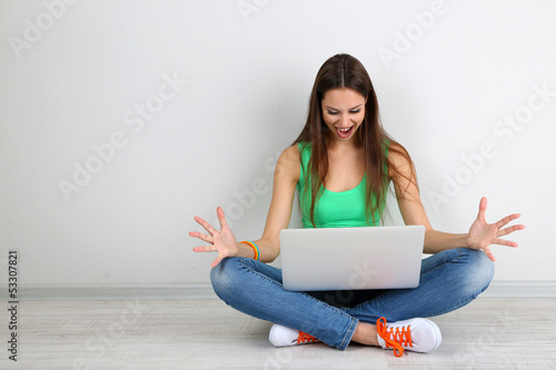 Photo: Beautiful young woman sitting with laptop in room Beautiful young woman sitting with laptop in room