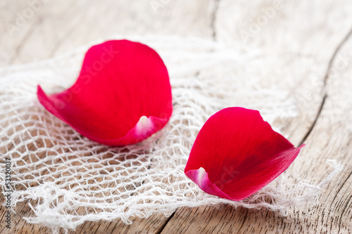 Photo: Two red rose petals on white cloth over wooden table Two red rose petals on white cloth over wooden table
