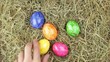 A hand cvollects a few estaer eggs from a pile of straw.