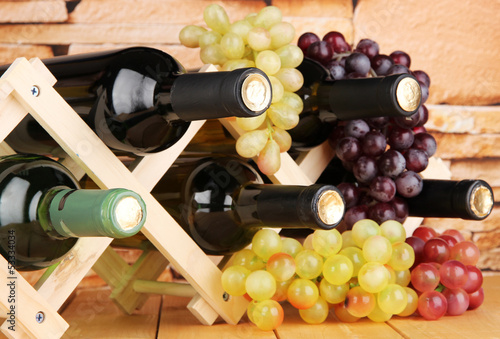 Photo: Bottles of wine placed on wooden stand on stone wall background Bottles of wine placed on wooden stand on stone wall background