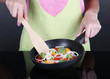 Hands cooking vegetable ragout in pan on gray background