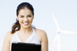 Teen girl with tablet computer next to wind turbine.