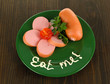 Sausage, greens, tomato on plate on wooden table