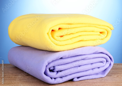 Photo: Warm plaids on wooden table, on blue background Warm plaids on wooden table, on blue background