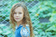 smiling little girl with curly hair near fence of grid