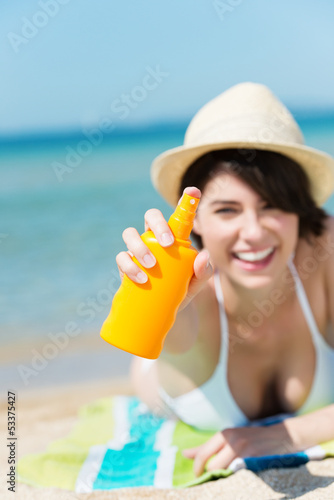 Photo: lachende frau am strand sprüht sonnencreme lachende frau am strand sprüht sonnencreme