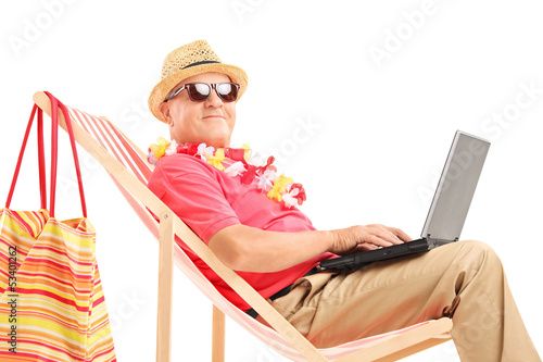 Photo: Mature male tourist on a sun lounger with a laptop Mature male tourist on a sun lounger with a laptop
