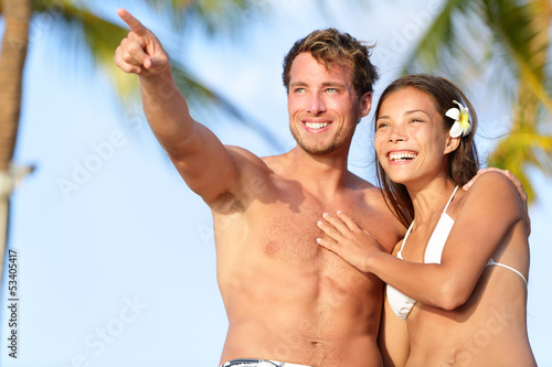 Photo: Couple on beach happy in swimwear, man pointing Couple on beach happy in swimwear, man pointing