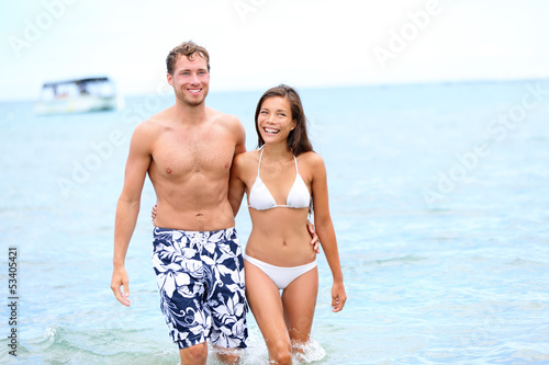Photo: Beach couple in love walking happy in water Beach couple in love walking happy in water