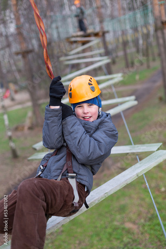 Photo: Little climber goes zigzag obstacle holding safety rope Little climber goes zigzag obstacle holding safety rope