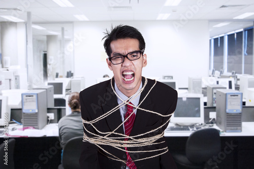 Photo: Angry businessman tied with rope at office Angry businessman tied with rope at office
