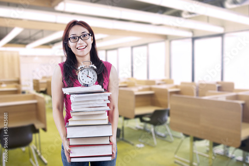 Photo: Happy female student bring stack of books and clock Happy female student bring stack of books and clock