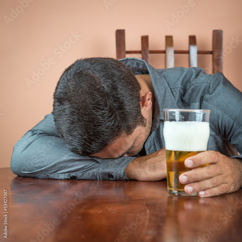 Photo: Drunk man sleeping on a table and holding a pint of beer Drunk man sleeping on a table and holding a pint of beer