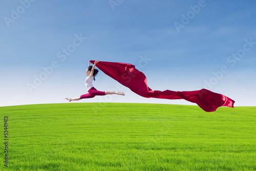 Photo: Beautiful female jumping with red scarf on field Beautiful female jumping with red scarf on field