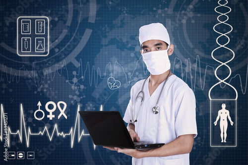 Photo: Doctor holding laptop on digital background Doctor holding laptop on digital background