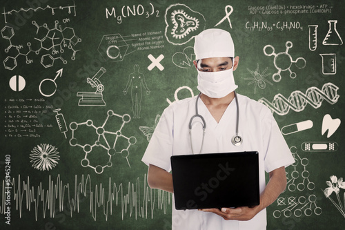 Photo: Health practitioner hold laptop on drawn chalkboard Health practitioner hold laptop on drawn chalkboard