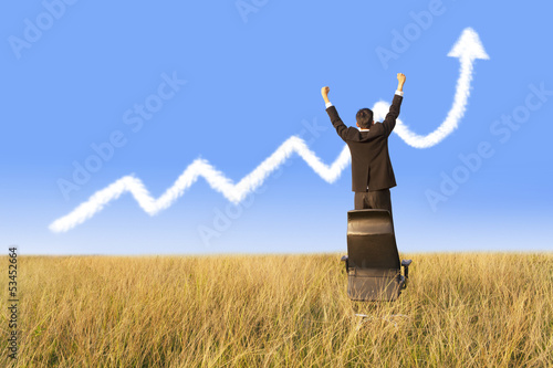 Photo: Businessman standing on chair with growing graph cloud Businessman standing on chair with growing graph cloud