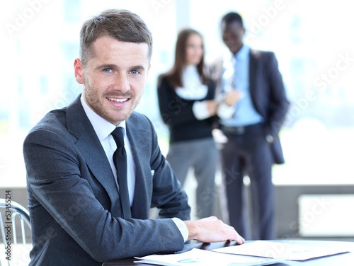Photo: Happy business man with team mates discussing in the background Happy business man with team mates discussing in the background