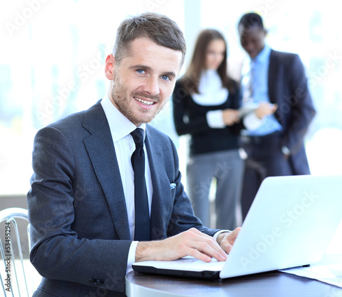 Photo: Business man sitting at his desk in the office with a laptop Business man sitting at his desk in the office with a laptop