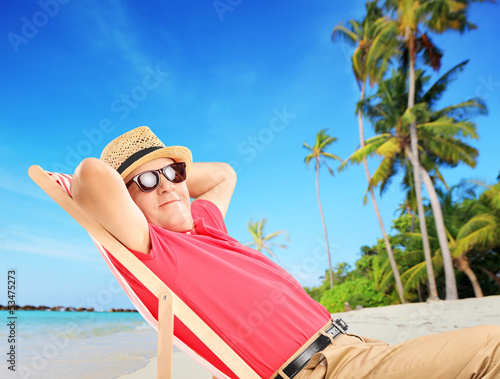 Photo: Mature male tourist enjoying on a beach next to a sea and palm t Mature male tourist enjoying on a beach next to a sea and palm t