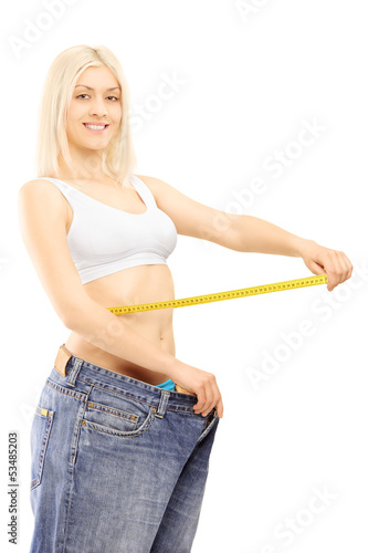 Photo: Smiling weightloss woman in old pairs of jeans measuring her wai Smiling weightloss woman in old pairs of jeans measuring her wai