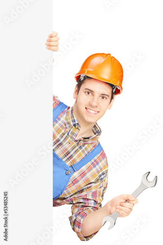 Photo: Young manual worker with helmet holding a wrench and posing behi Young manual worker with helmet holding a wrench and posing behi