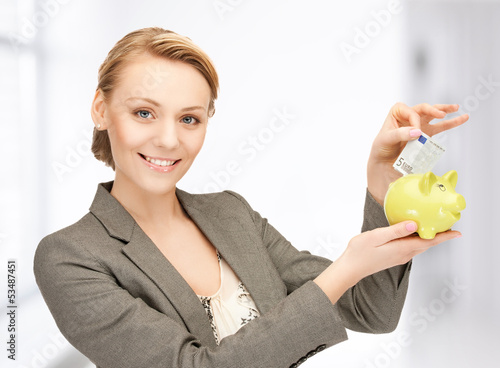 Photo: woman putting cash money into small piggy bank woman putting cash money into small piggy bank