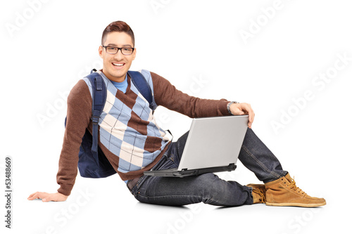 Photo: Smiling handsome guy sitting on a floor with laptop and looking Smiling handsome guy sitting on a floor with laptop and looking
