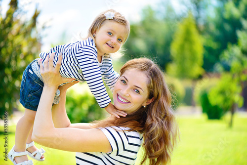 Photo: Young mother and cute daughter with blue eyes playing at park Young mother and cute daughter with blue eyes playing at park