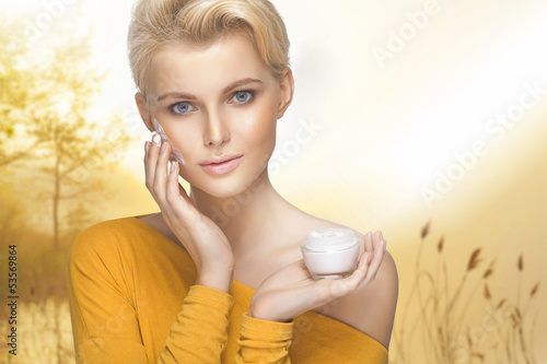 Photo: Portrait of young woman applying moisturizer cream on her pretty Portrait of young woman applying moisturizer cream on her pretty