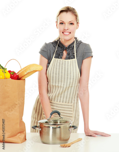 Photo: Woman in apron standing near table with grocery bag Woman in apron standing near table with grocery bag