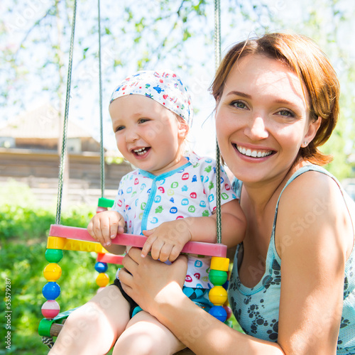 Photo: Happy mother with laughing baby sits on swing Happy mother with laughing baby sits on swing