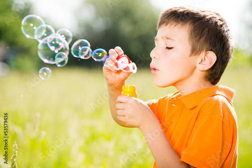 Photo: Young caucasian boy blowing the soap bubbles on nature Young caucasian boy blowing the soap bubbles on nature