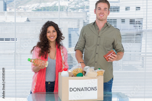 Photo: Smiling volunteers taking out food from donations box Smiling volunteers taking out food from donations box