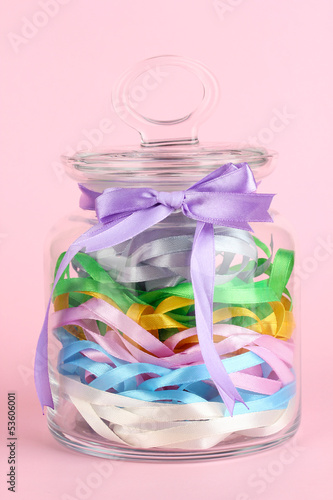 Photo: Glass jar containing various colored ribbons on pink background Glass jar containing various colored ribbons on pink background