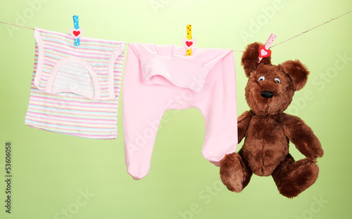 Photo: Baby clothes hanging on clothesline, on color background Baby clothes hanging on clothesline, on color background