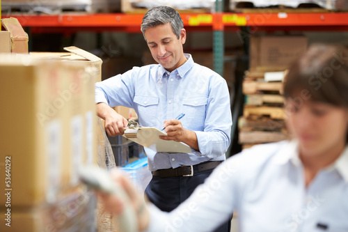 Photo: Manager In Warehouse With Worker Scanning Box In Foreground Manager In Warehouse With Worker Scanning Box In Foreground