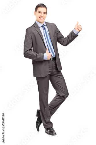 Photo: Young businessman leaning against wall and giving thumb up Young businessman leaning against wall and giving thumb up