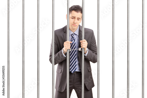 Photo: Handcuffed businessman in suit posing in jail and holding bars Handcuffed businessman in suit posing in jail and holding bars
