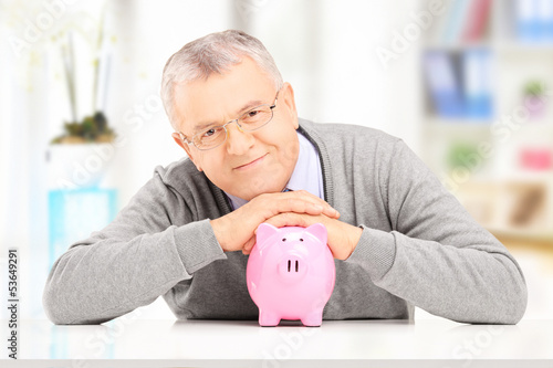 Photo: Satisfied gentleman posing over a piggy bank at his home Satisfied gentleman posing over a piggy bank at his home