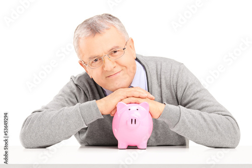 Photo: Satisfied mature gentleman posing over a piggy bank Satisfied mature gentleman posing over a piggy bank