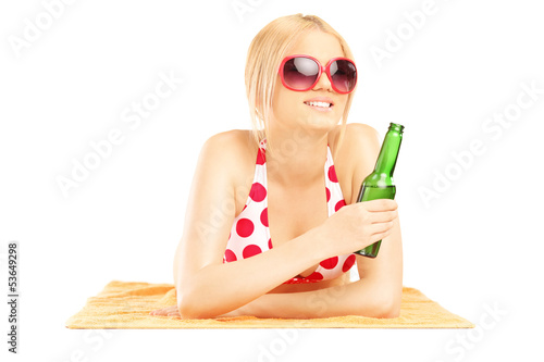 Photo: Smiling beautiful female lying on a towel and drinking beer Smiling beautiful female lying on a towel and drinking beer