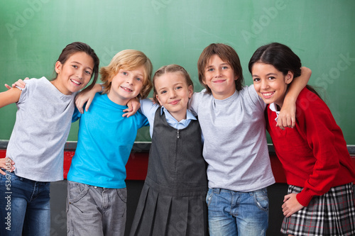 Photo: Cute Schoolchildren With Arms Around Standing Together In Classr Cute Schoolchildren With Arms Around Standing Together In Classr