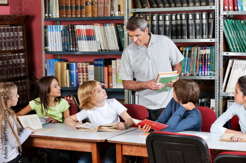 Photo: Teacher Communicating With Students Sitting At Table In Library Teacher Communicating With Students Sitting At Table In Library