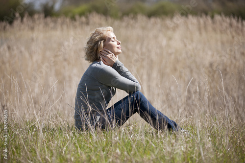 Photo: A mature woman sitting on the grass, enjoying the sunshine A mature woman sitting on the grass, enjoying the sunshine