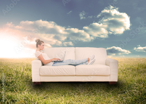 Photo: Woman using laptop on couch in field Woman using laptop on couch in field